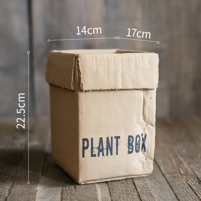 Cement flower pot with brown paper box texture and drainage holes, shown in a neutral home setting.
