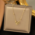 Gold coloured titanium steel necklace with a bow charm on a cross chain.