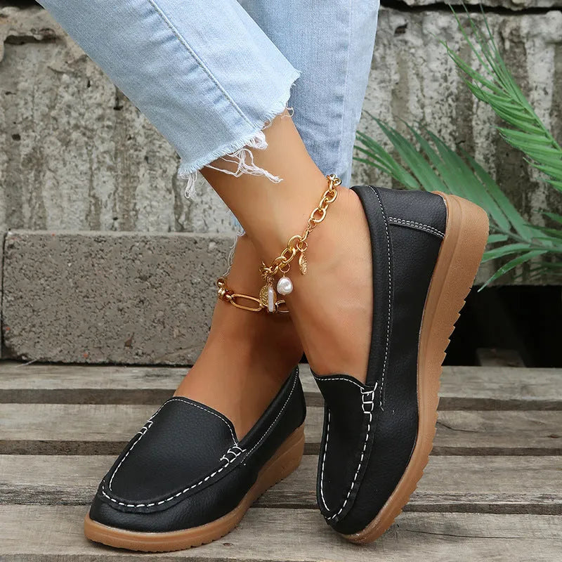 Women's flat slip-on loafers in PU leather, showing colour options and round toe design with decorative stitching.