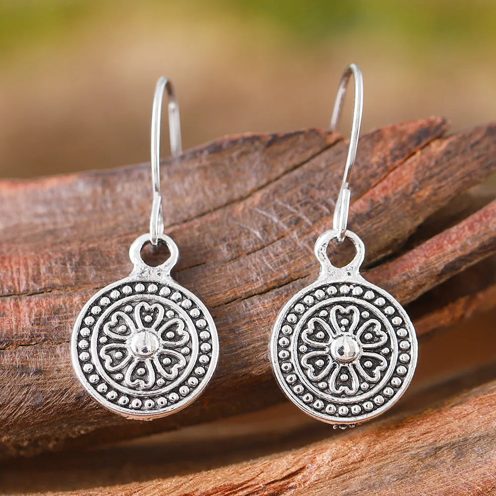 Close-up of a pair of distressed geometric bohemian earrings with a round print, in zinc alloy with electroplated colour.