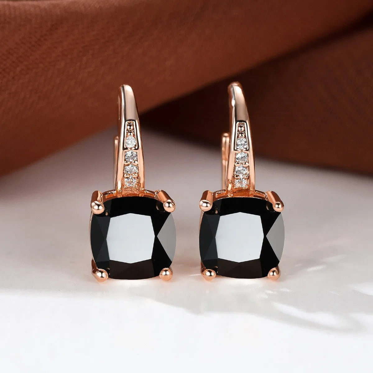 Geometric copper ear hook with round element and inlaid square zircon stone, shown in a golden colour.