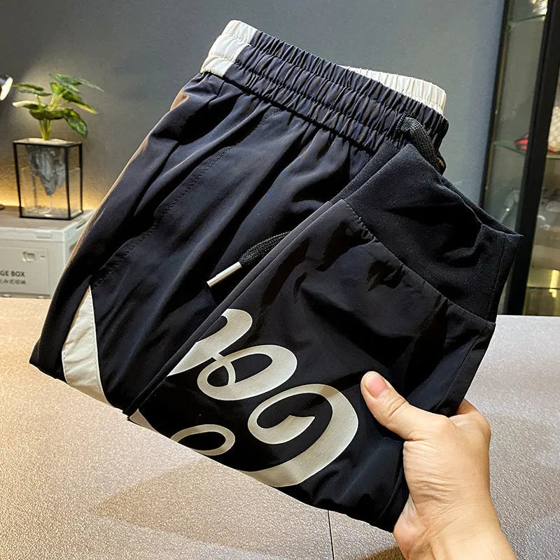 Men's black ice silk ankle banded cropped casual trousers on a plain background.