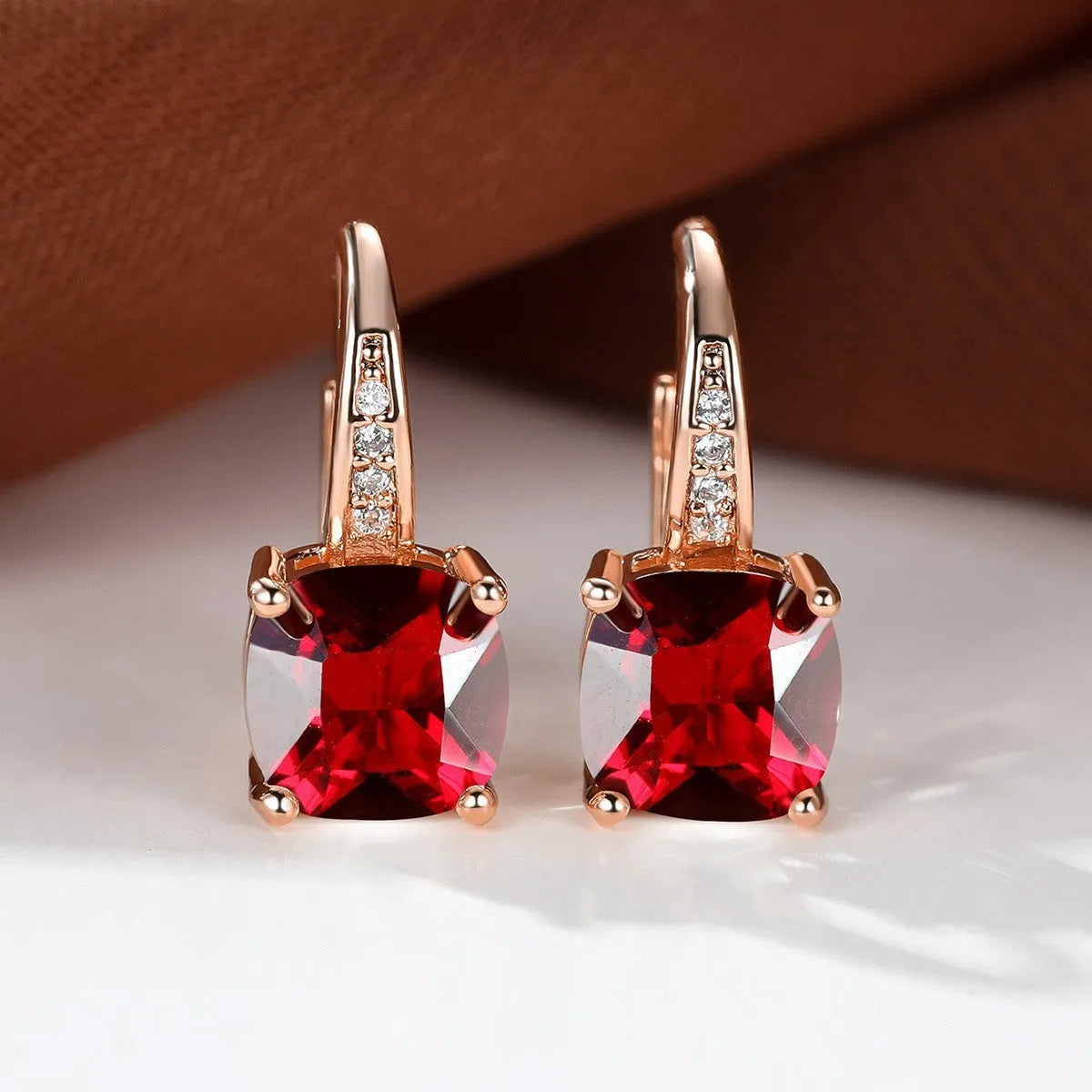 Geometric copper ear hook with round element and inlaid square zircon stone, shown in a golden colour.