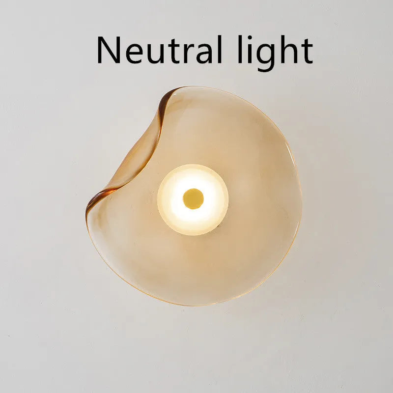 Round glass wall lamp in cognac colour mounted beside a bed with warm light illumination