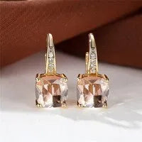 Geometric copper ear hook with round element and inlaid square zircon stone, shown in a golden colour.