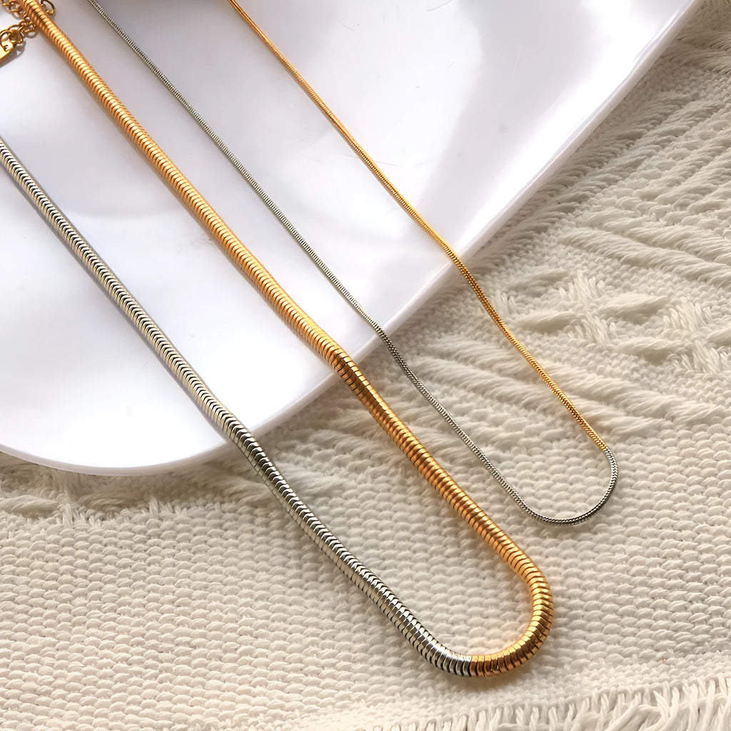 Close-up of a women's gold 3mm snake bone chain necklace with a geometric pendant.