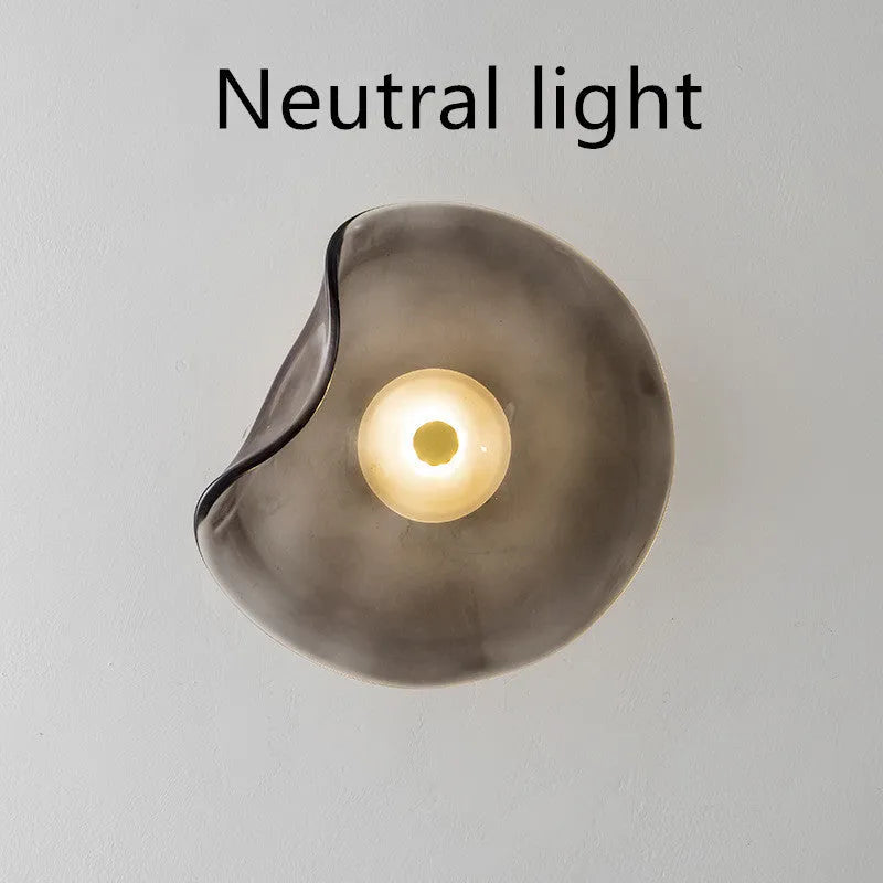Round glass wall lamp in cognac colour mounted beside a bed with warm light illumination