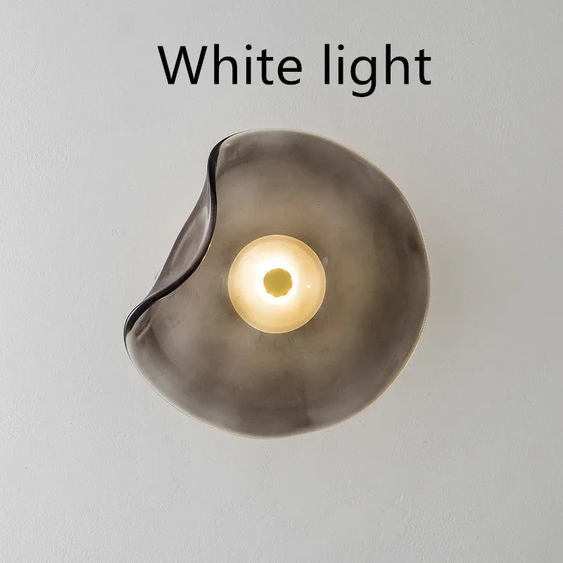 Round glass wall lamp in cognac colour mounted beside a bed with warm light illumination