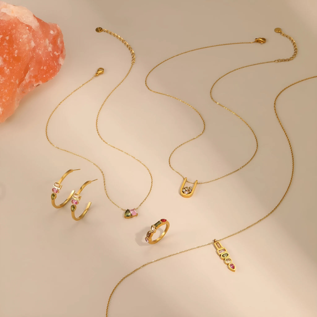 Geometric gold plated zircon necklace, ring, and earrings set on a plain background