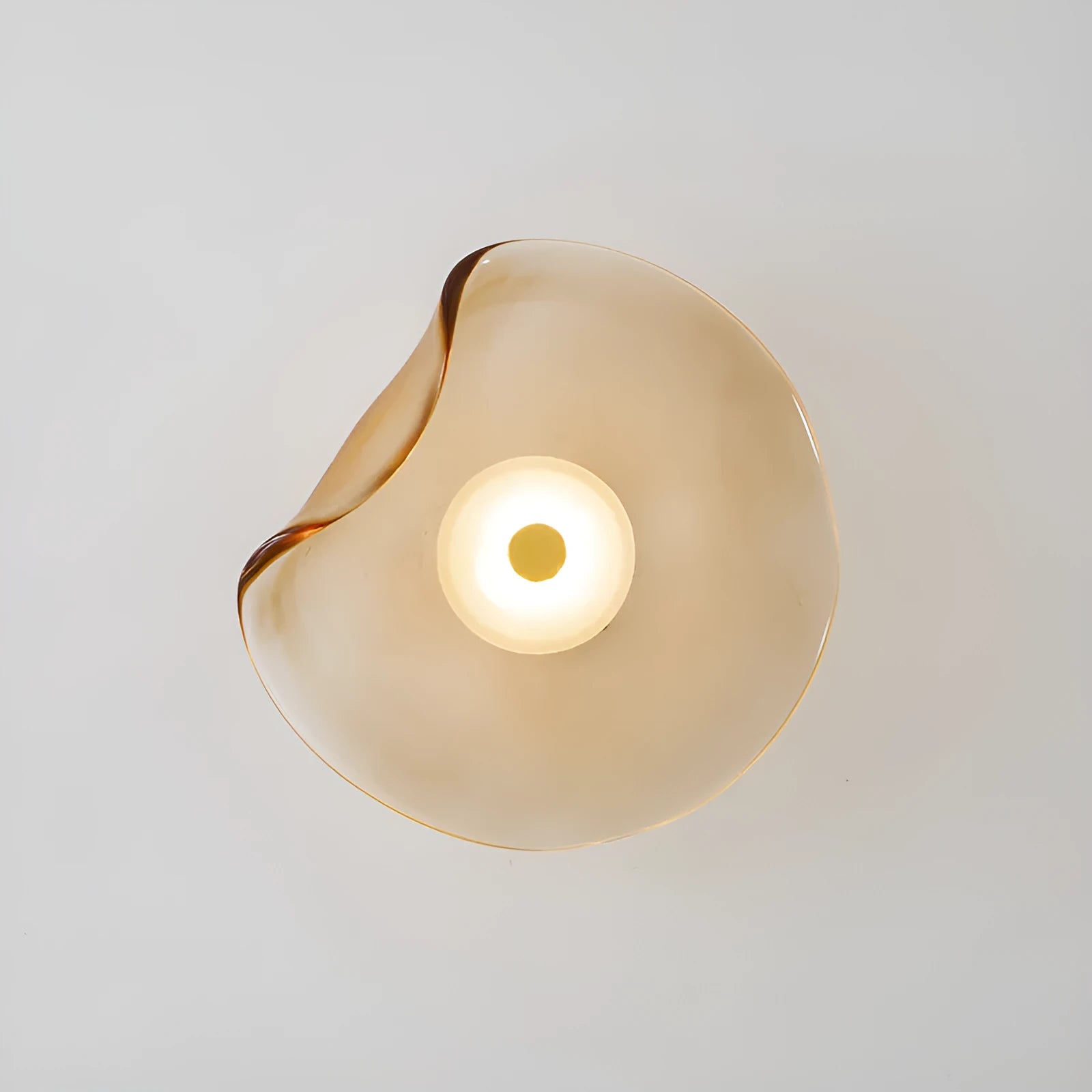 Round glass wall lamp in cognac colour mounted beside a bed with warm light illumination