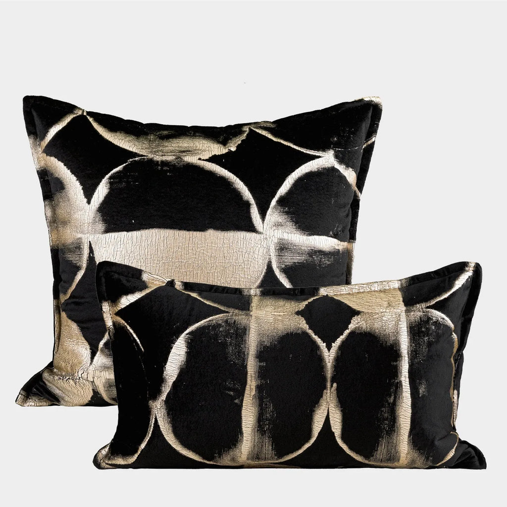 Black gold abstract patterned square decorative pillow with a soft flannel texture on a grey sofa.
