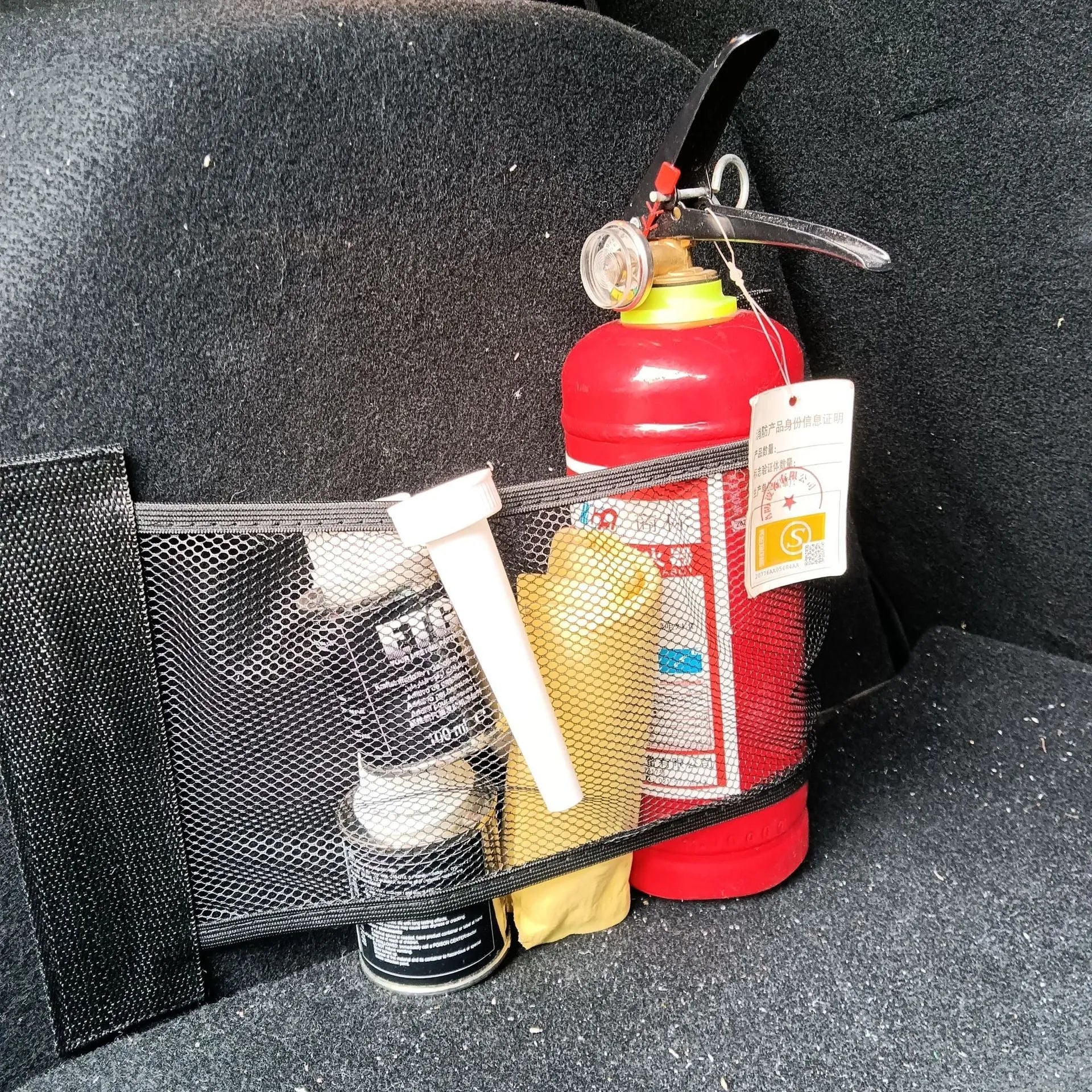 Black elastic polyester storage net stretched in a car boot, holding a water bottle and cloth.