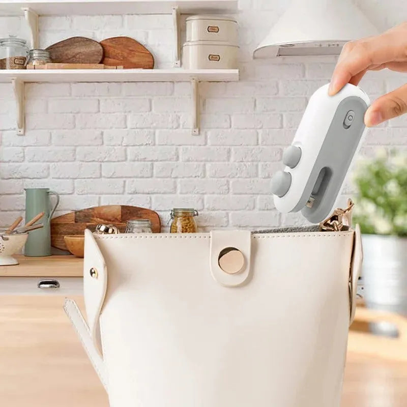 White and blue handheld USB heat sealer with cutter blade on a kitchen counter.