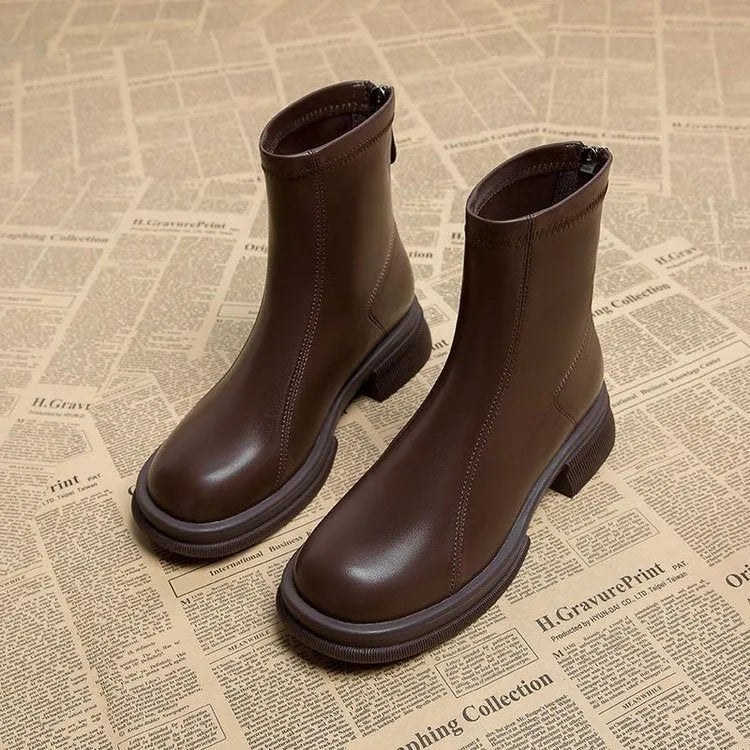 Women's black ankle boots with flat heel, round toe, and back zip fastening on wooden floor
