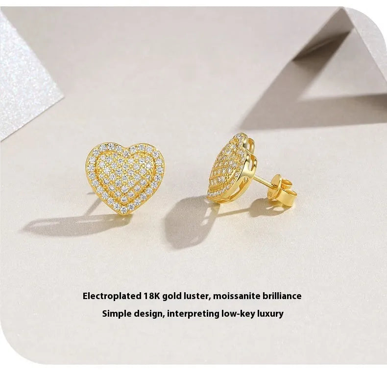A pair of gold-coloured heart-shaped moissanite stud earrings on a plain background.