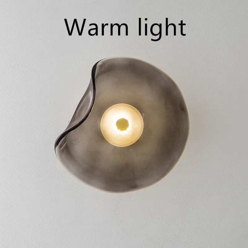 Round glass wall lamp in cognac colour mounted beside a bed with warm light illumination