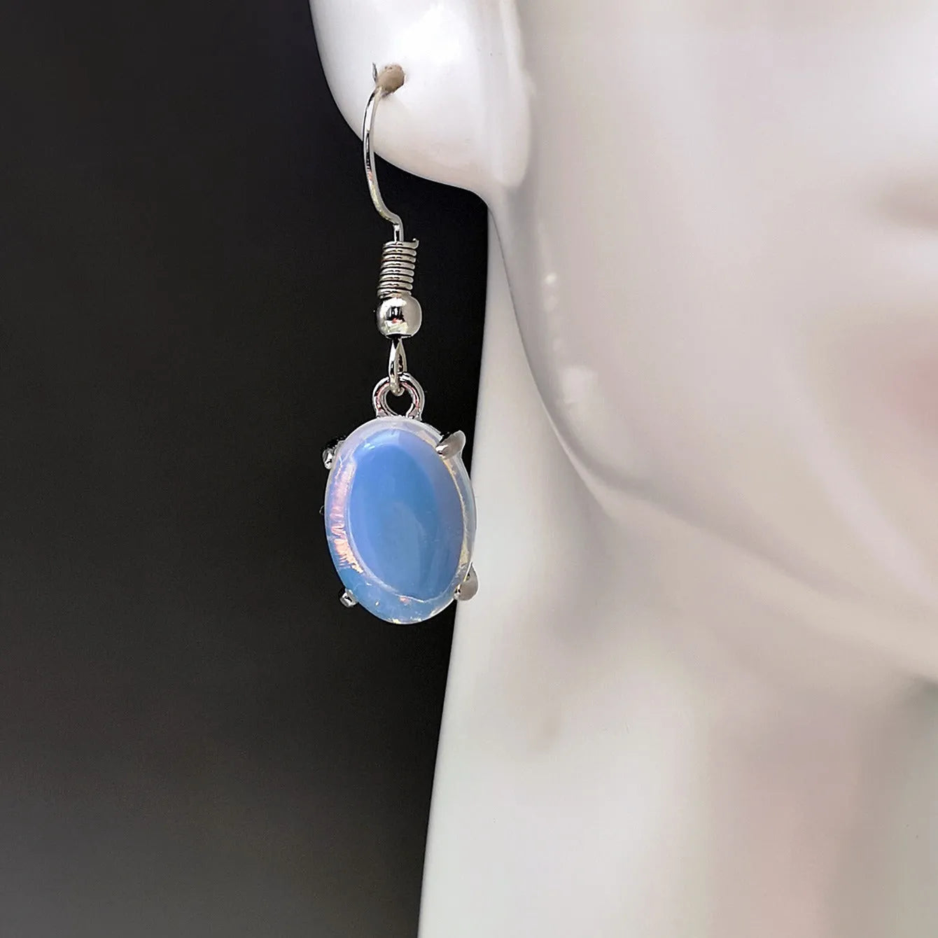 A pair of retro drop-shaped earrings with a cross design in moonlight opal colour on a white background.