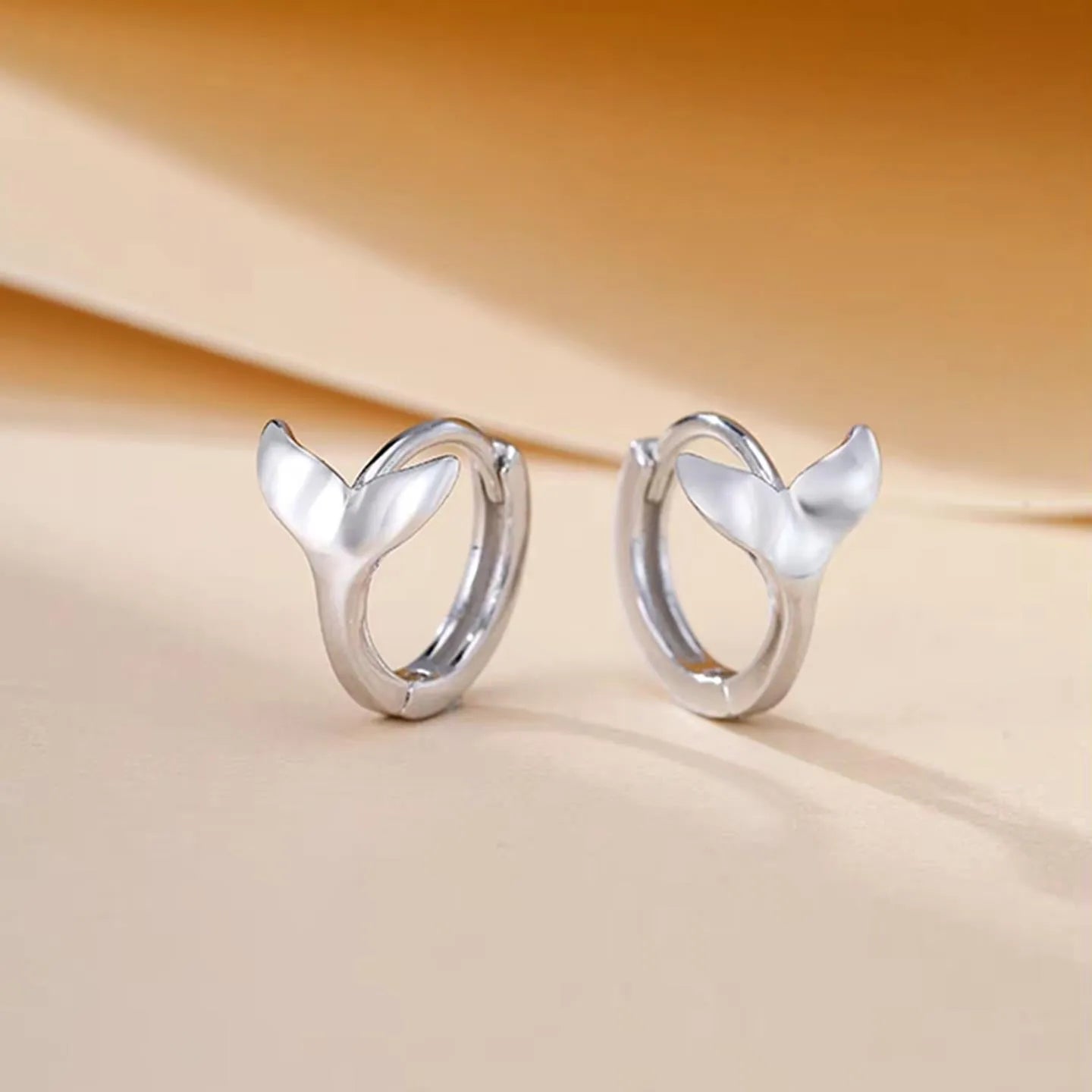 Women's fishtail design earrings in electroplated White Gold colour on a white background.
