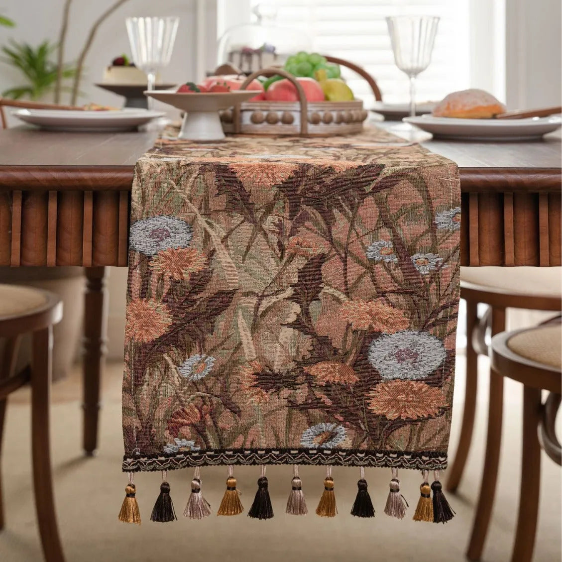 Beige Jacquard table runner with long fabric tassels and floral leaf pattern laid on a wooden table.