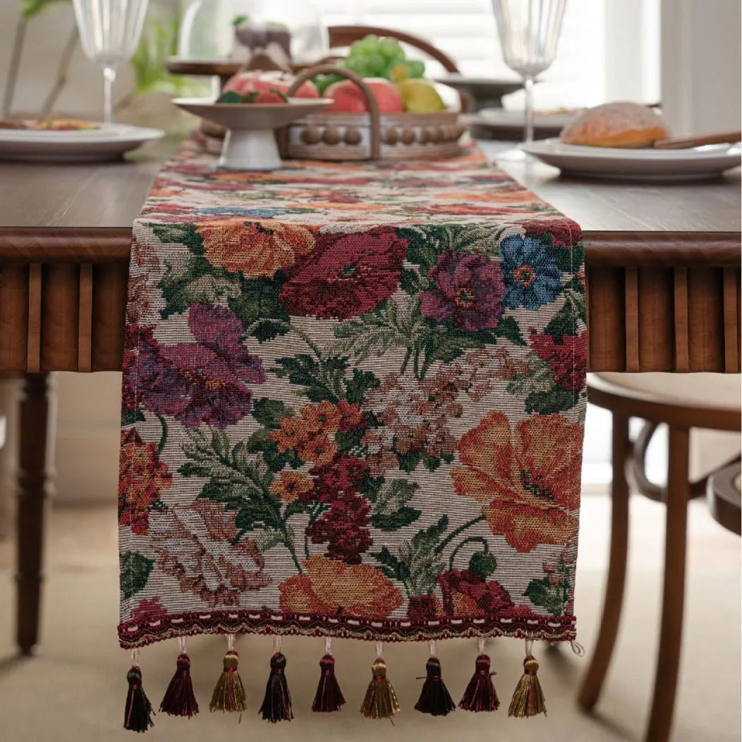 Beige Jacquard table runner with long fabric tassels and floral leaf pattern laid on a wooden table.