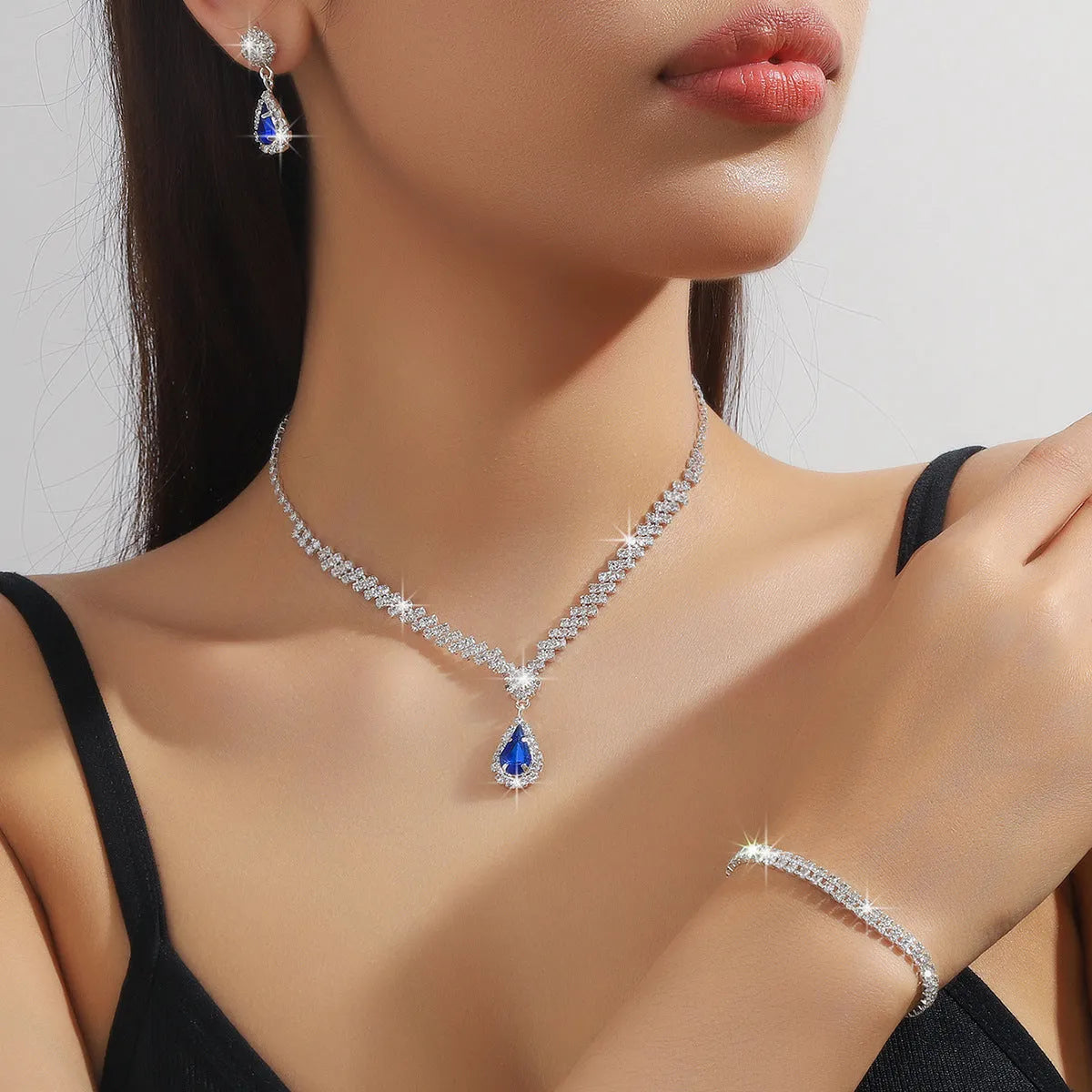 Women's rhinestone water drop necklace and earrings set on a claw chain in blue colour.