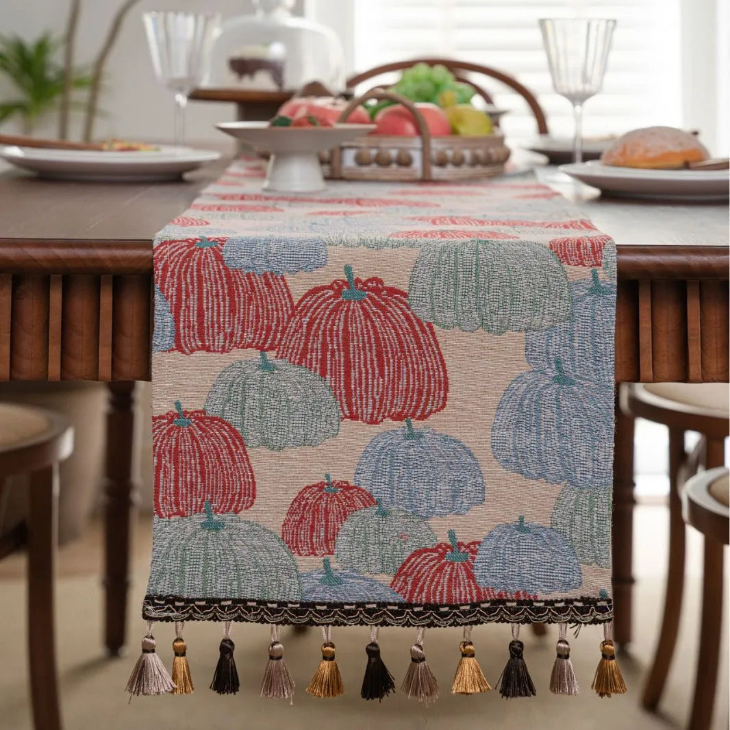 Beige Jacquard table runner with long fabric tassels and floral leaf pattern laid on a wooden table.