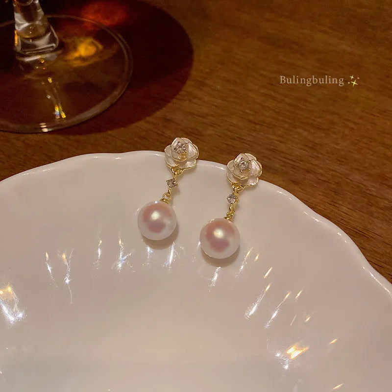 A pair of alloy camellia flower stud earrings for women with a faux pearl centre.