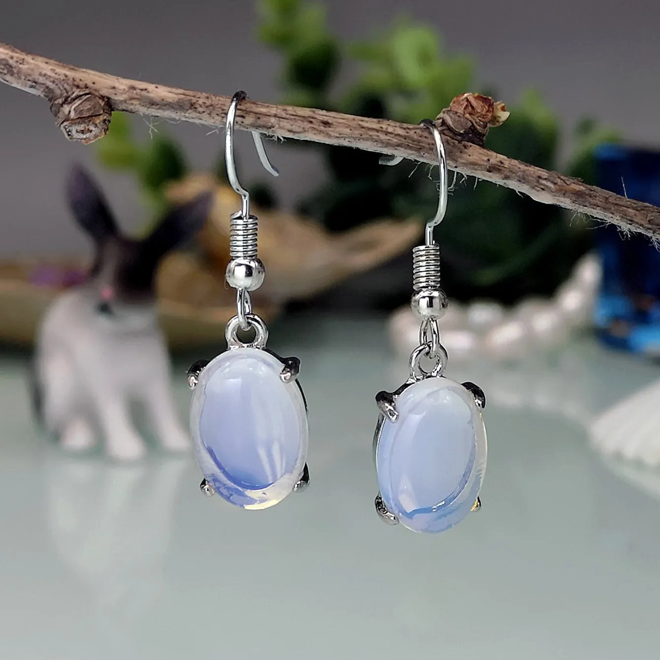 A pair of retro drop-shaped earrings with a cross design in moonlight opal colour on a white background.