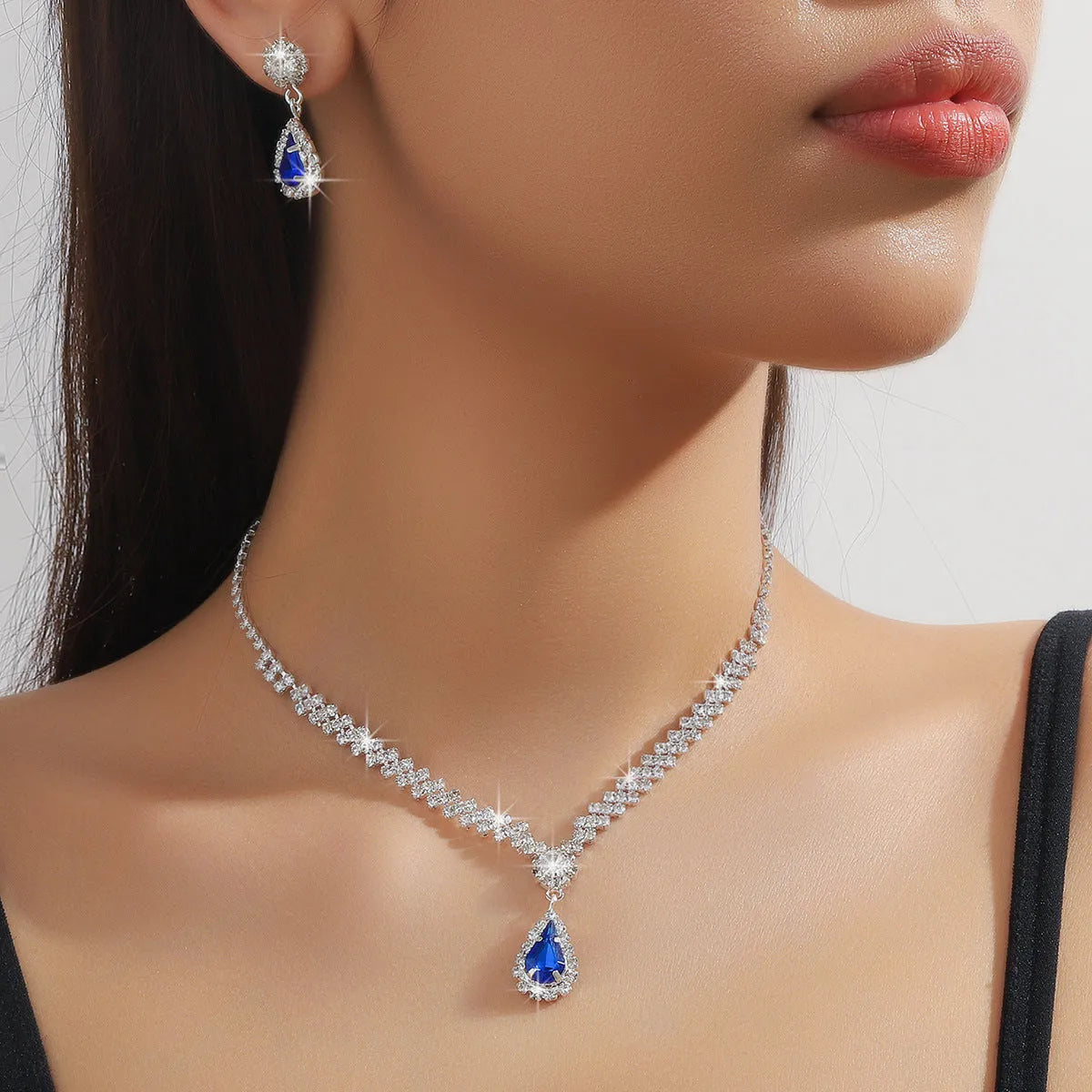 Women's rhinestone water drop necklace and earrings set on a claw chain in blue colour.