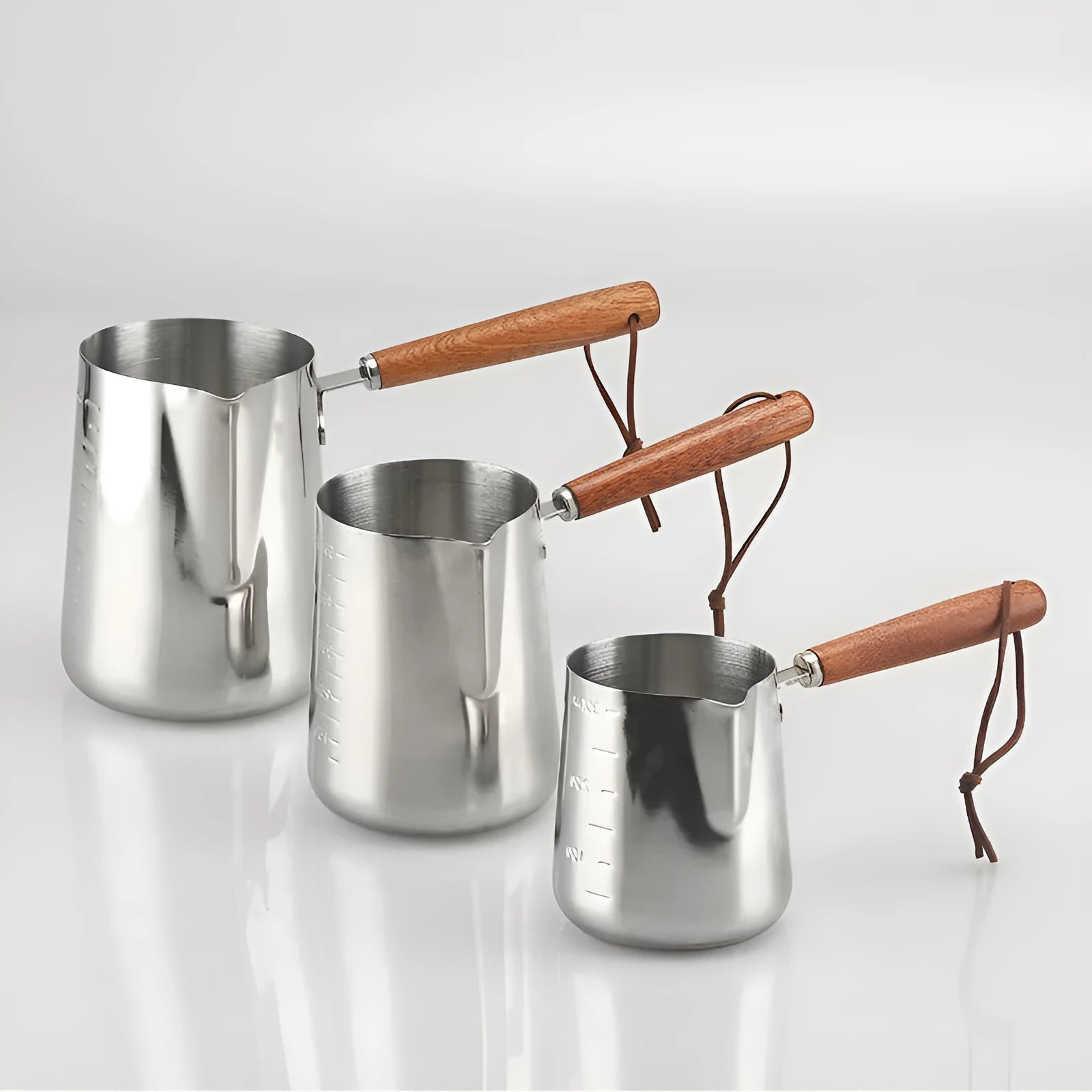 Stainless steel barista milk jug with measurement scale and wooden handle shown in 350ml, 600ml, and 1000ml sizes.
