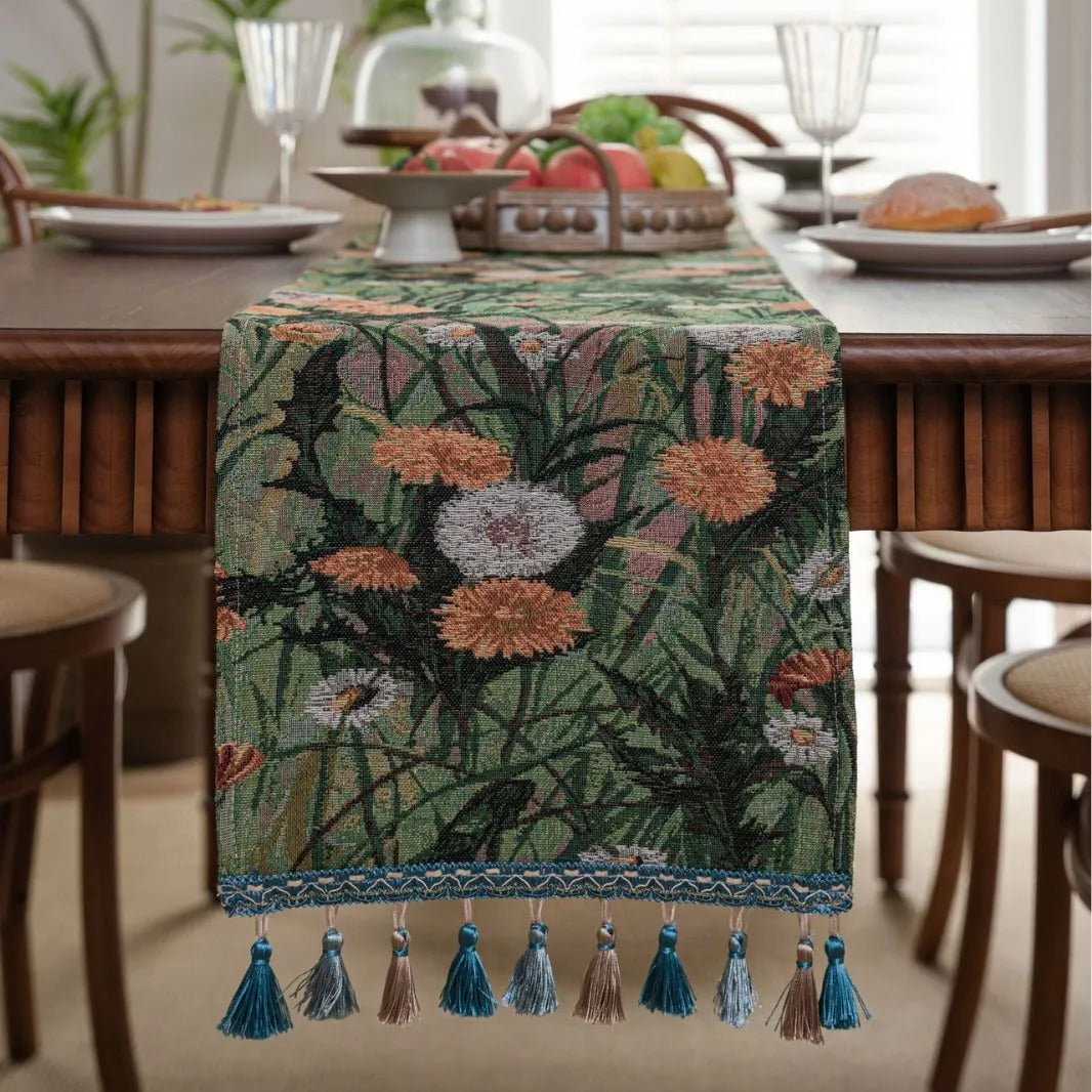 Beige Jacquard table runner with long fabric tassels and floral leaf pattern laid on a wooden table.