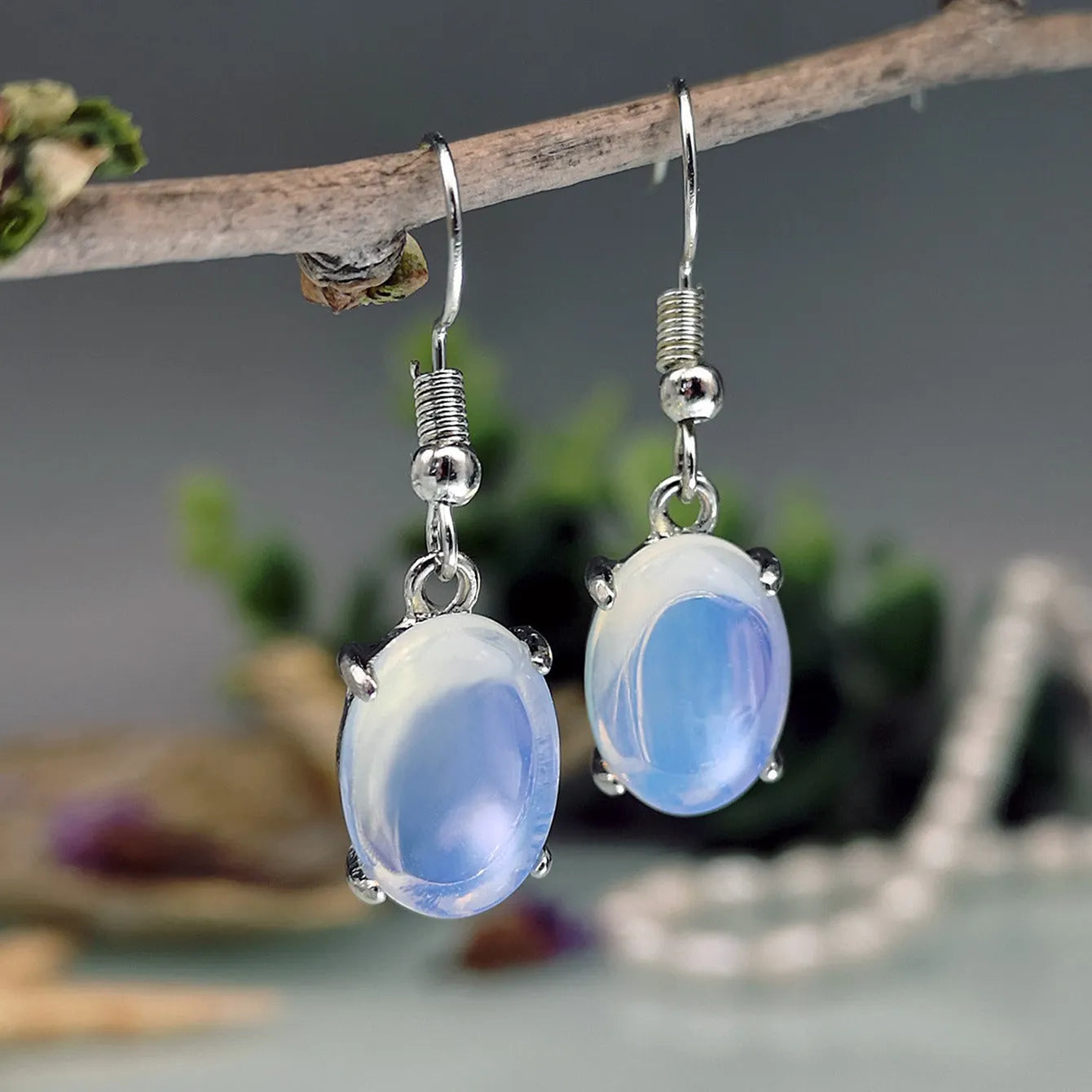 A pair of retro drop-shaped earrings with a cross design in moonlight opal colour on a white background.