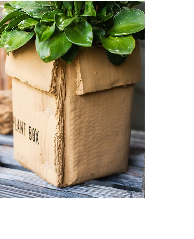 Cement flower pot with brown paper box texture and drainage holes, shown in a neutral home setting.