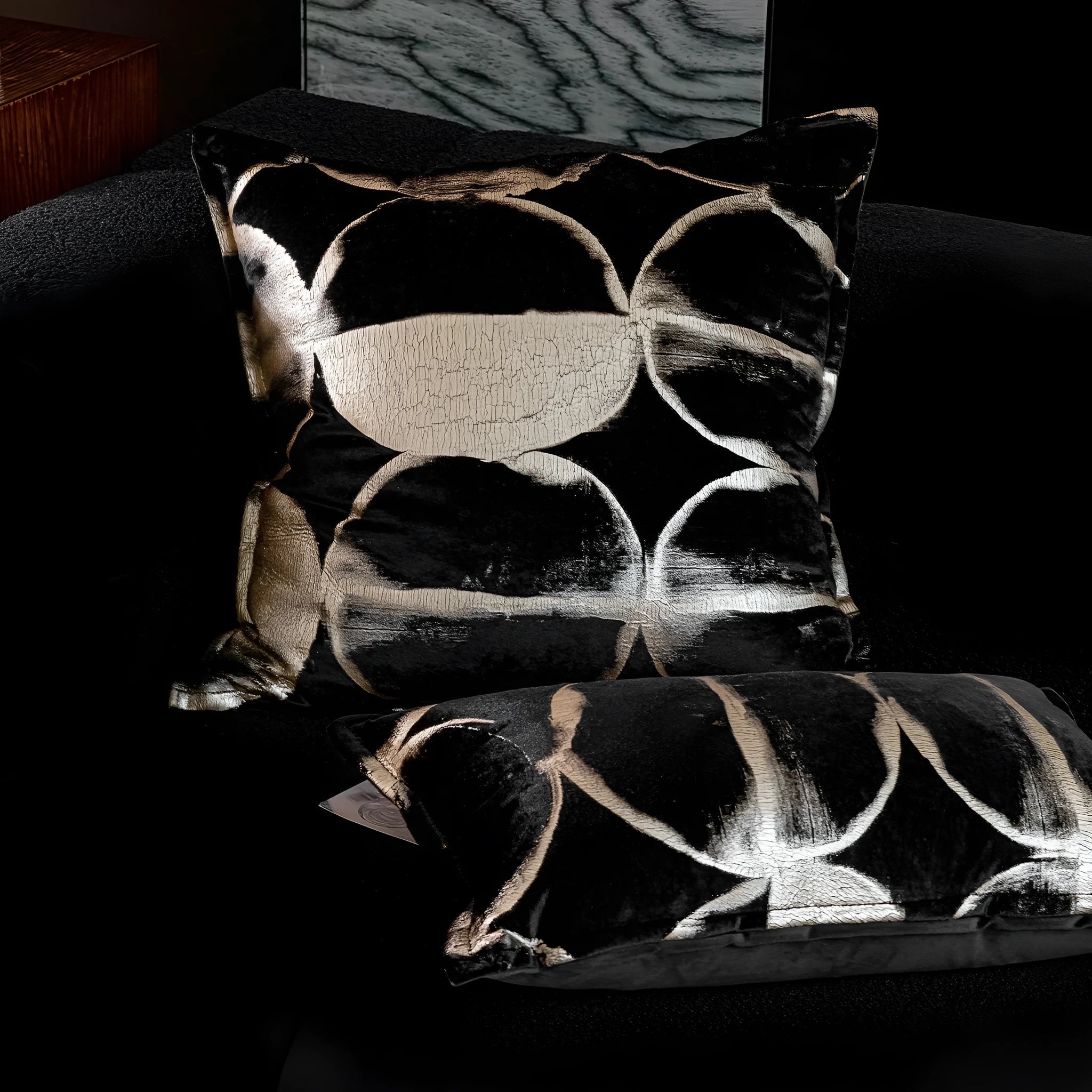 Black gold abstract patterned square decorative pillow with a soft flannel texture on a grey sofa.