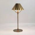 Gold alloy desk lamp with a cylindrical shade, shown lit with warm white light on a wooden desk.