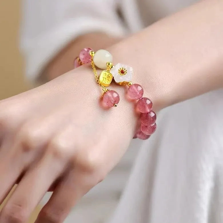 Handmade strawberry quartz crystal bracelet with Hetian jade peach blossom charm on a wrist.