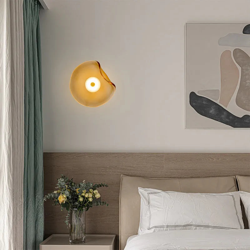 Round glass wall lamp in cognac colour mounted beside a bed with warm light illumination