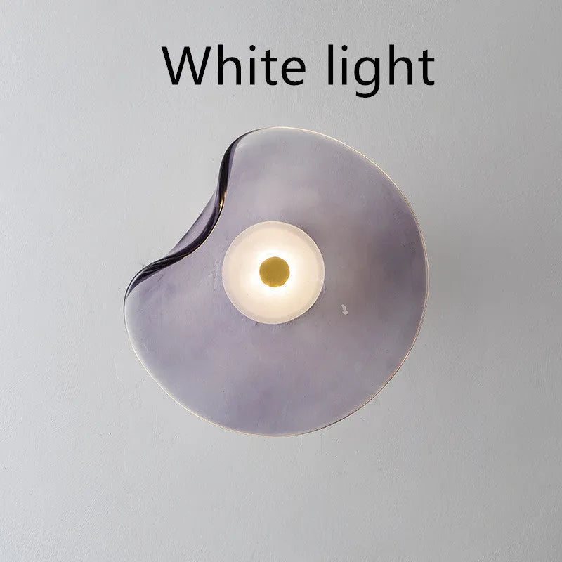 Round glass wall lamp in cognac colour mounted beside a bed with warm light illumination