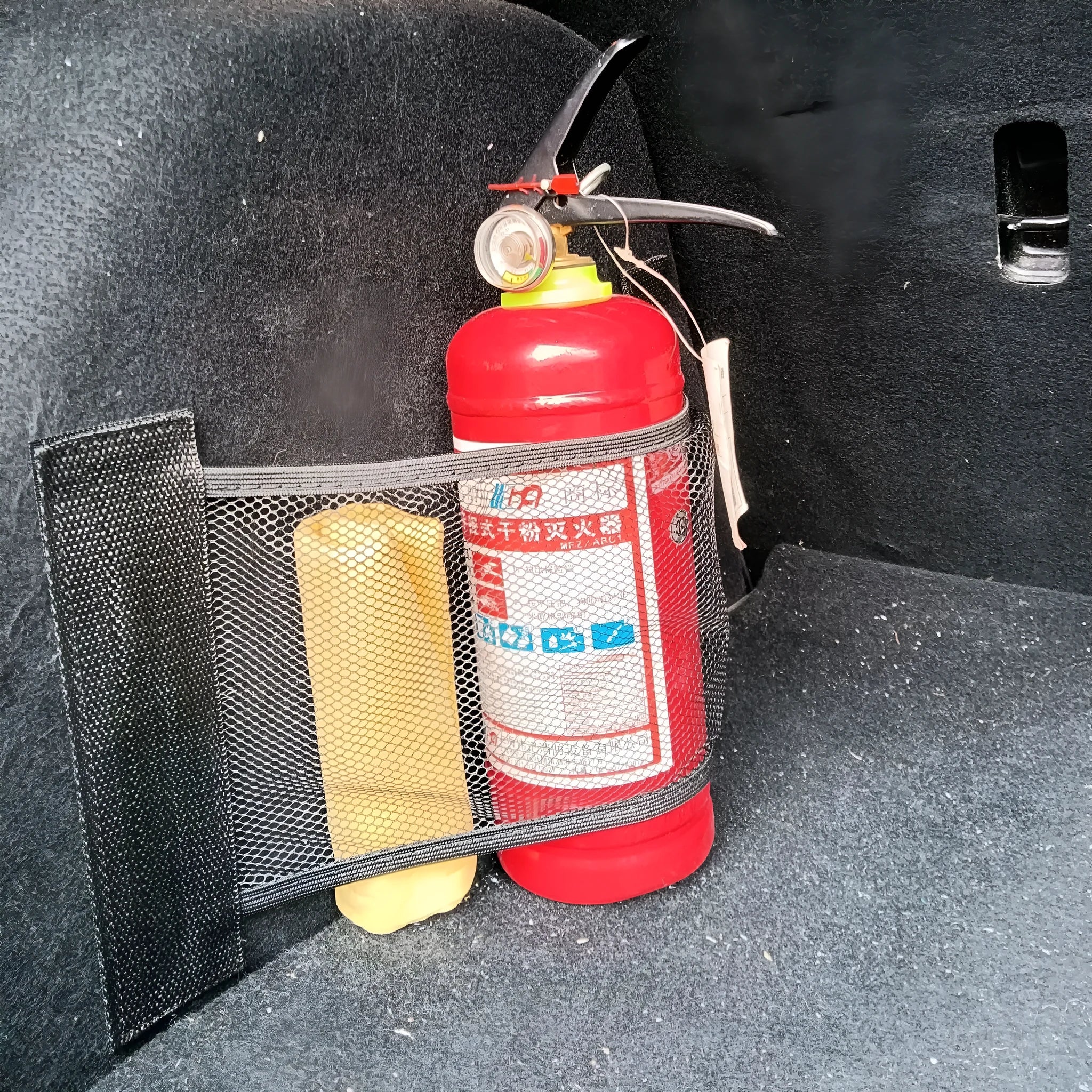 Black elastic polyester storage net stretched in a car boot, holding a water bottle and cloth.