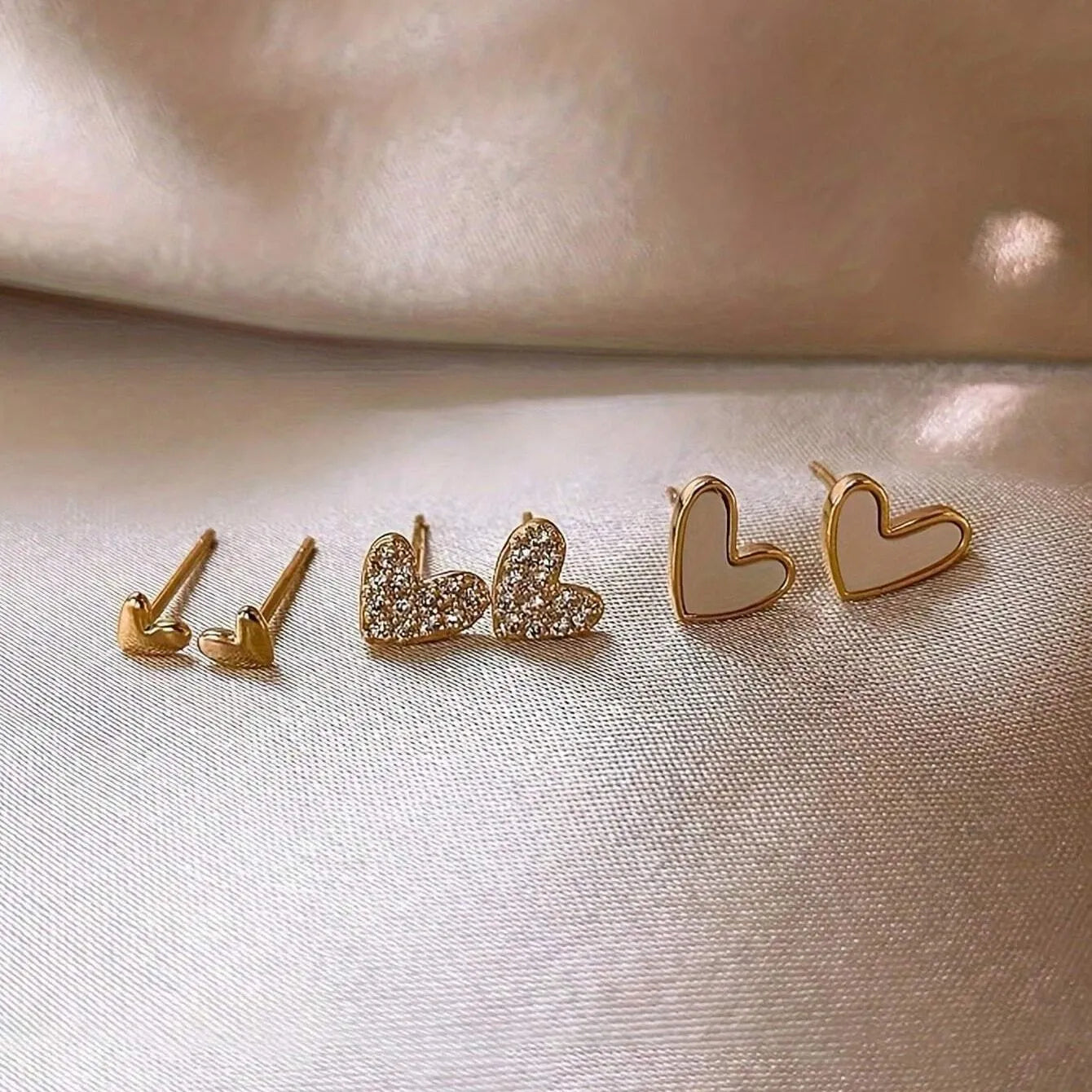 Three pairs of heart-shaped alloy earrings in gold, black, and pink with electroplated finish