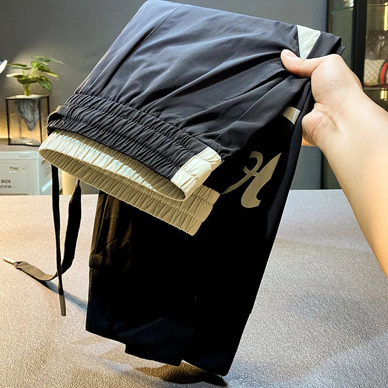 Men's black ice silk ankle banded cropped casual trousers on a plain background.