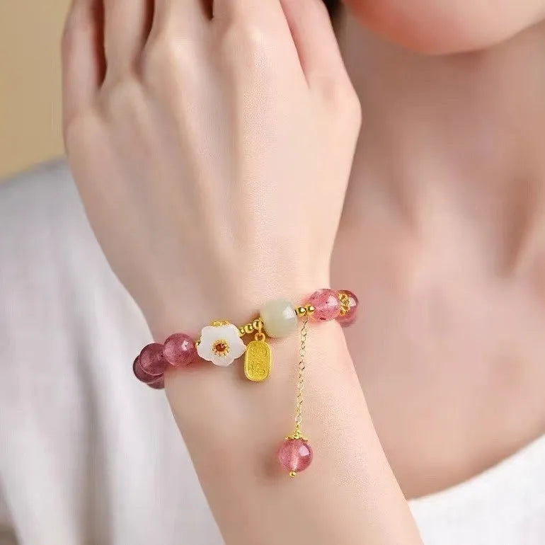 Handmade strawberry quartz crystal bracelet with Hetian jade peach blossom charm on a wrist.