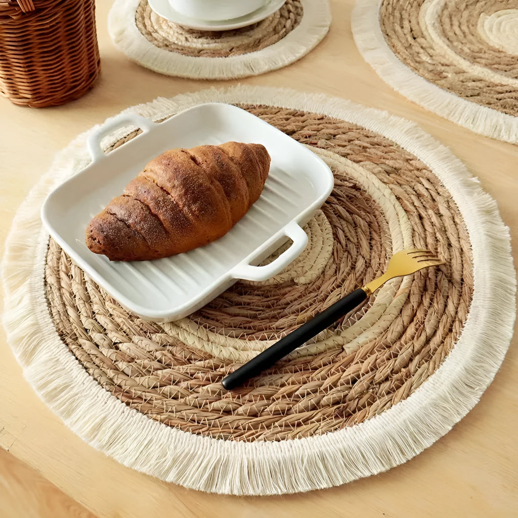 Round natural papyrus straw placemat with tassel edge on a wooden table.
