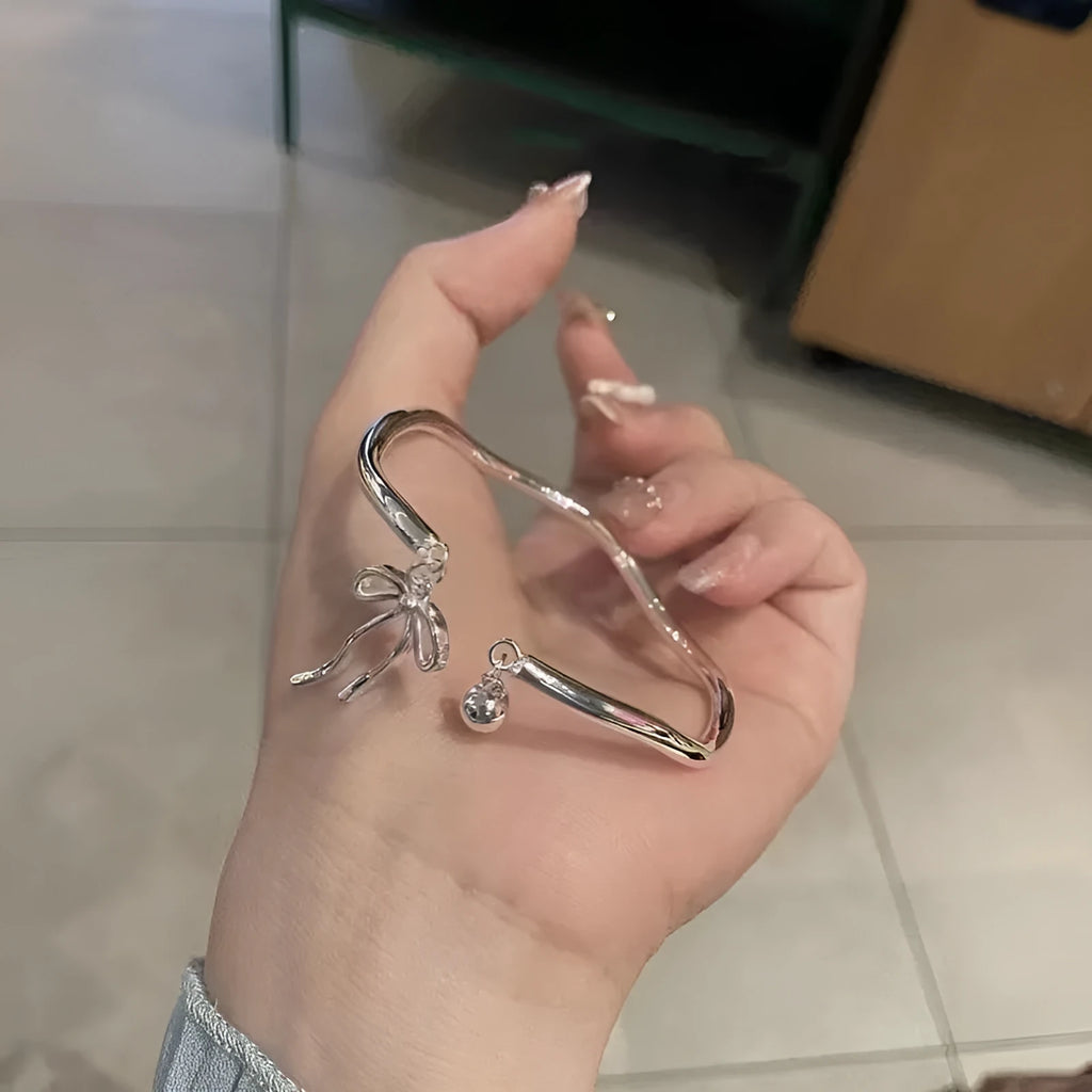 Silver adjustable bracelet with bow charm featuring bell opening detail