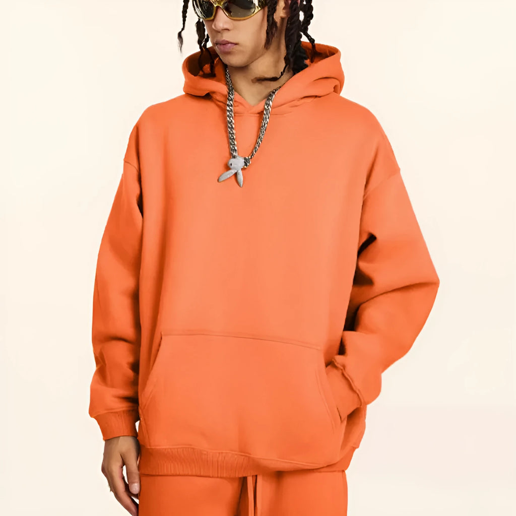 A man wearing a loose-fit, 450g cotton, hooded pullover sweater in a neutral colour with drop-shoulder sleeves.