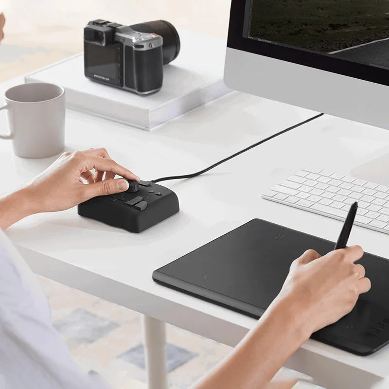 TourBox NEO black creative controller for video editing on a desk next to a tablet.