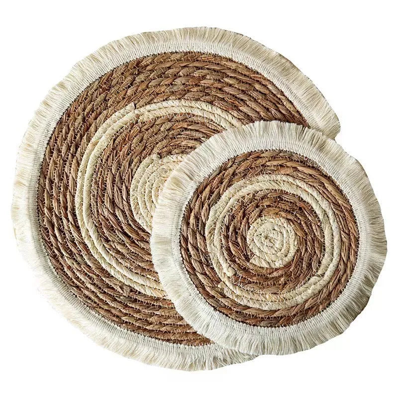 Round natural papyrus straw placemat with tassel edge on a wooden table.