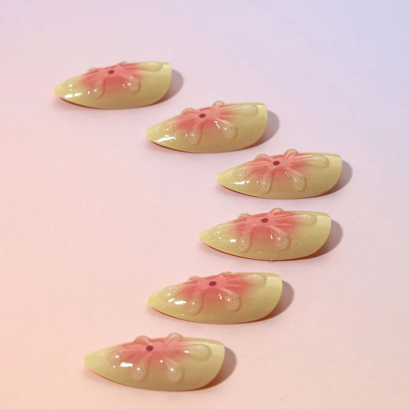 Plastic false nails with white cartoon 3D flower decoration, pot of jelly glue, and nail file on pink background.