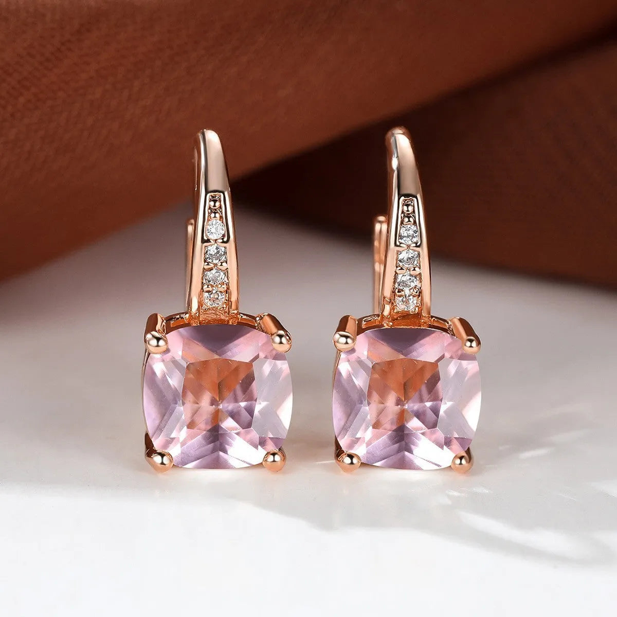 Geometric copper ear hook with round element and inlaid square zircon stone, shown in a golden colour.