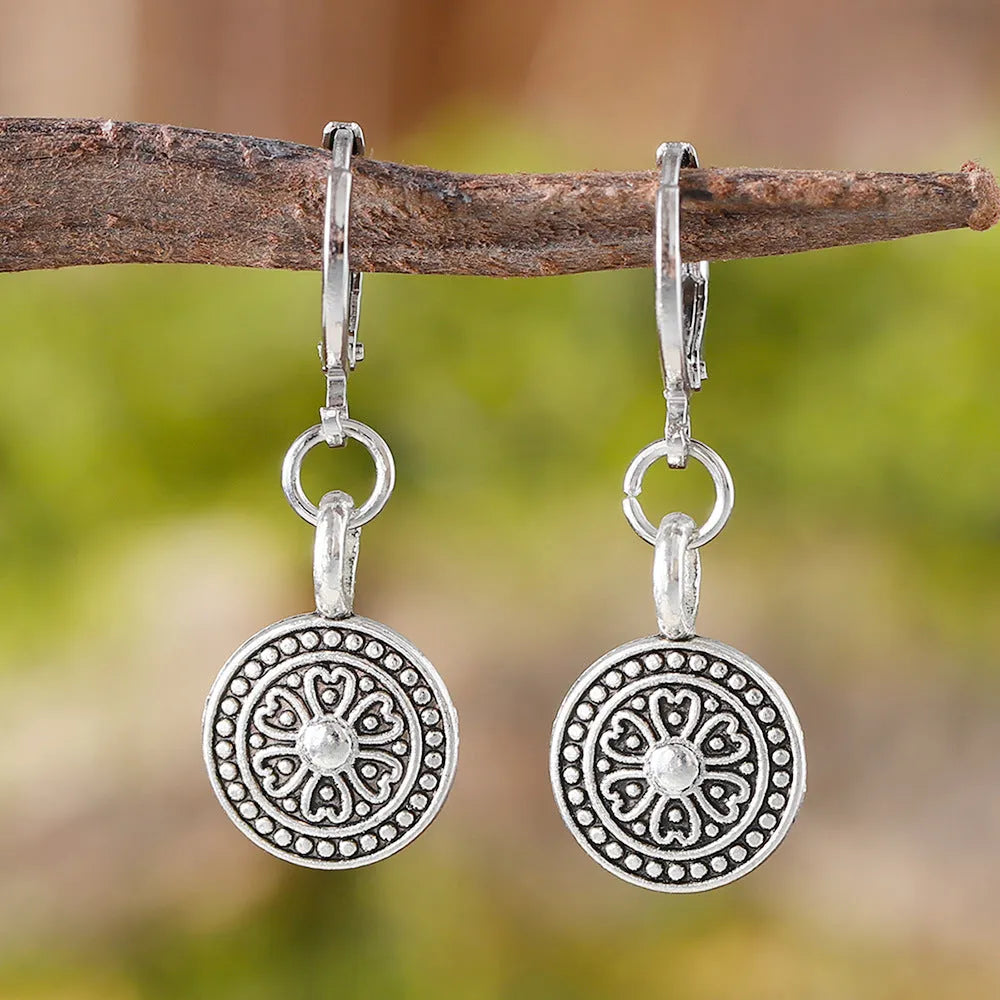 Close-up of a pair of distressed geometric bohemian earrings with a round print, in zinc alloy with electroplated colour.